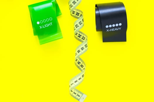 Two fitness tapes of black and green color are located at the top of the photo on a yellow background, top view, flat lay, copy space, isolate. High quality photo