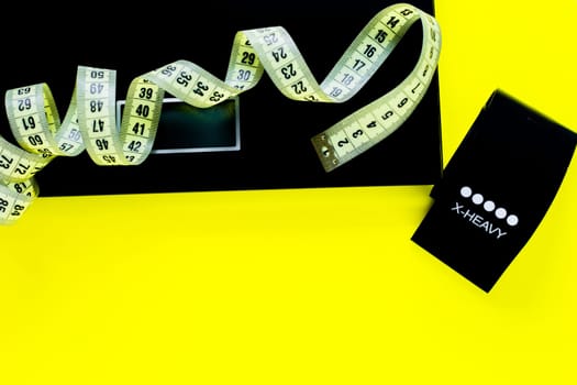 A weight scale, a black fitness tape and a yellow measuring tape lie on a yellow background on top of the photo. top view, flat lay, copy space, isolate. High quality photo