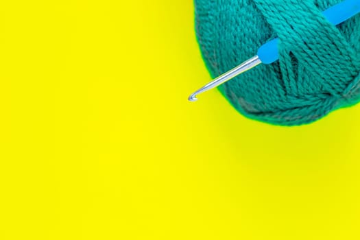 A metal hook with a blue handle is inserted into a skein of green yarn in the upper corner of the photo on a yellow background. top view, flat lay, copy space, isolate. High quality photo