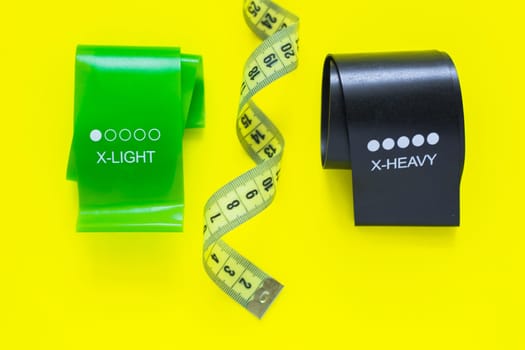 Two fitness tapes of black and green color are located at the top of the photo on a yellow background, they are separated by a yellow measuring tape. top view, flat lay, copy space, isolate. High quality photo