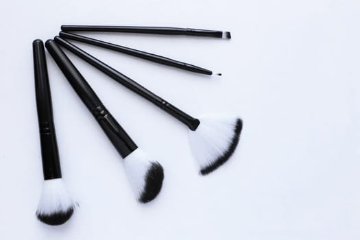Black brushes with white and black pile for makeup of different sizes lie on a white background, they lie like a fan in the corner. top view, flat lay, copy space, isolate. High quality photo