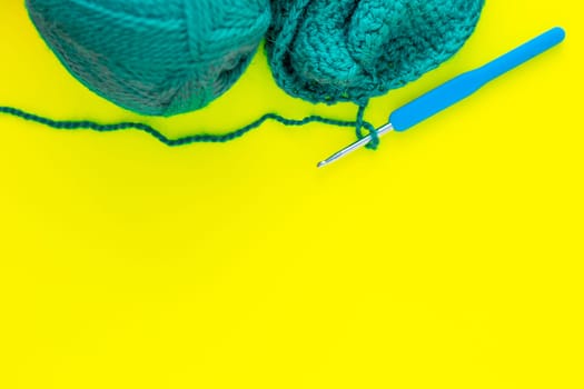 A metal hook with a blue handle, a skein of green yarn and a part of a knitted fragment lies on top of the photo on a yellow background. top view, flat lay, copy space, isolate. High quality photo