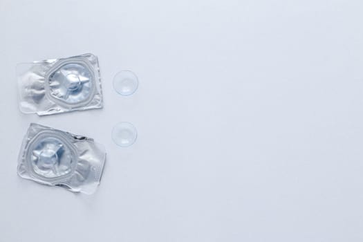 Two contact lenses in a closed package and two open contact lenses lie on the side on a white background with space for text. top view, flat lay, copy space, isolate. High quality photo