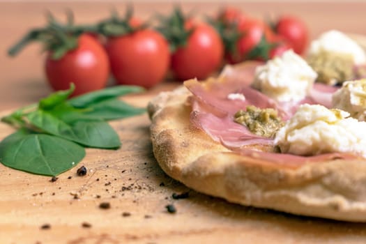 Close up of italian pizza on a wooden cutting board. On background defocused tomatoes and basil.