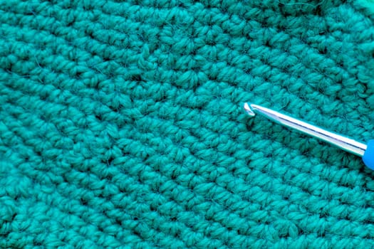 A metal hook with a blue handle lies on a knitted fragment of green color. High quality photo
