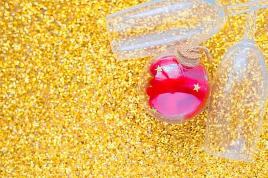 Two champagne glasses are lying in the corner of the picture, between them is a red Christmas ball on a gold textured background. top view, flat lay, copy space, isolate. High quality photo