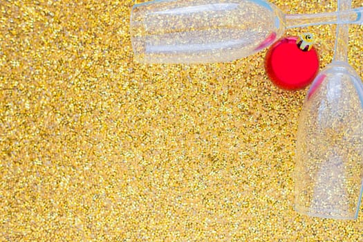 Two champagne glasses are lying in the corner of the picture, between them is a red Christmas ball on a gold textured background. top view, flat lay, copy space, isolate. High quality photo