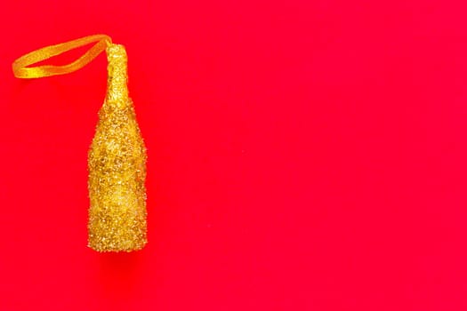 A toy for the Christmas tree in the form of a golden champagne bottle with sequins lies on the side on a red background. top view, flat lay, copy space, isolate. High quality photo