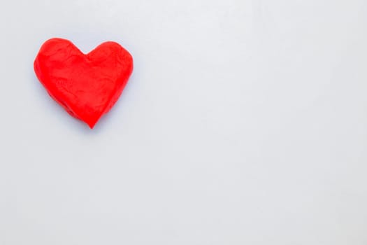 A heart made of red dough for modeling lies on the side of the photo. High quality photo