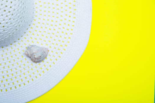 On a white sun hat with a wide brim there is a shell on a yellow background with a place for text. High quality photo