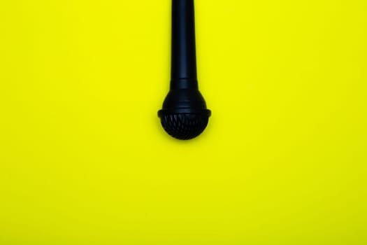 A black microphone hangs from above on a yellow background. High quality photo