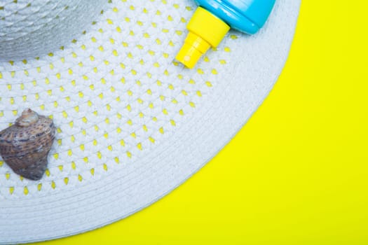 On a white sun hat with a wide brim there is a shell and a tanning agent on a yellow background with a place for text. High quality photo