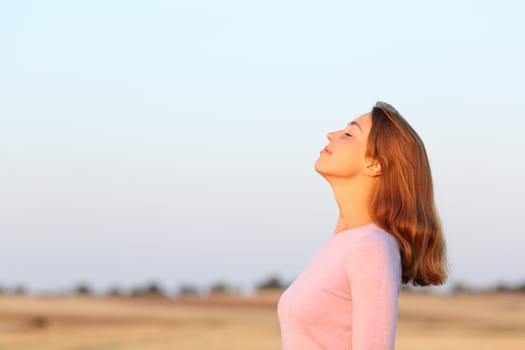 Side view portrait of a relaxed woman breathing fresh air at sunrise in a field