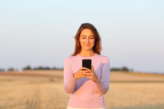 Front view of a happy woman using smart phone in harvested field