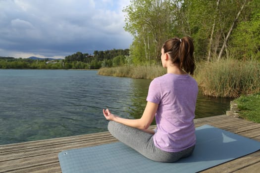 Yogi practicing yoga exercise sitting in a lake pier