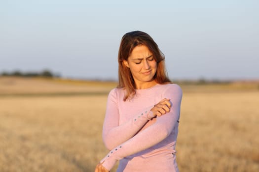 Stressed woman scratching itchy arm in a harvested field