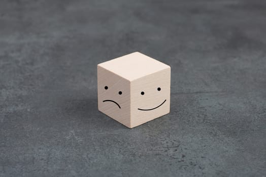 One wooden cube with a smiling and a sad face on a dark background, symbol