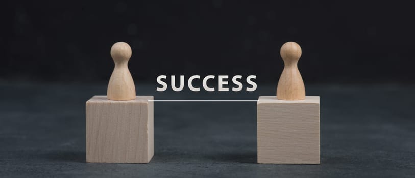 Two wooden people standing on cubes, connected through a line and the word success, dark background
