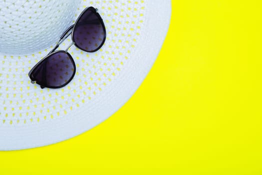 On a white sun hat with a wide brim are sunglasses on a yellow background with a place for text. High quality photo