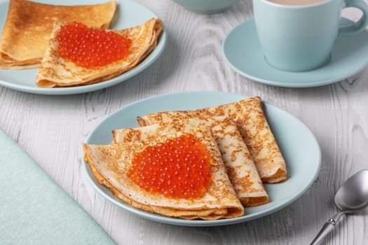 Savory crepes filled with fresh orange fish roe served on a light blue plate at a cozy breakfast table.