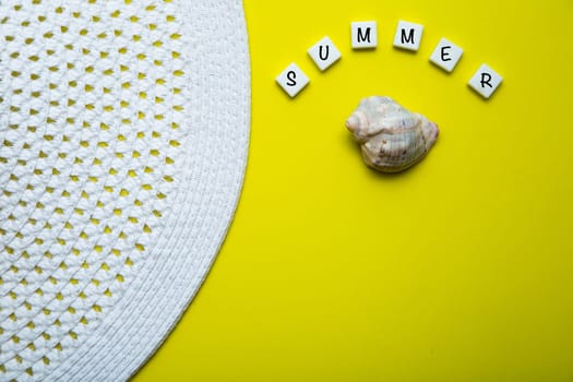On a yellow background there is a shell and the word summer is written above it, a summer hat is lying on the side. High quality photo