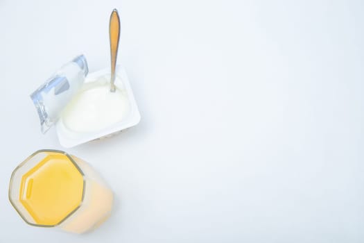 A cup of natural yogurt, a dessert spoon and a glass of orange juice on a white background. High quality photo