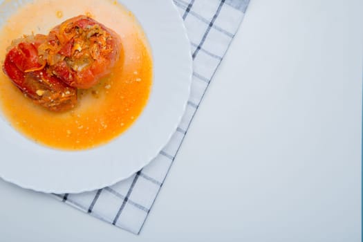 Red pepper stuffed with minced meat and carrots with onions lies on a white plate, which stands on a waffle napkin on a white background. High quality photo