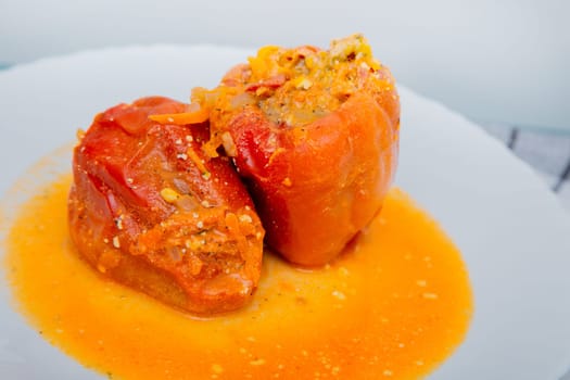 Red pepper stuffed with minced meat and carrots with onions lies on a white plate, which stands on a waffle napkin on a white background. High quality photo