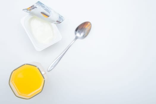 A cup of natural yogurt, a dessert spoon and a glass of orange juice on a white background. High quality photo