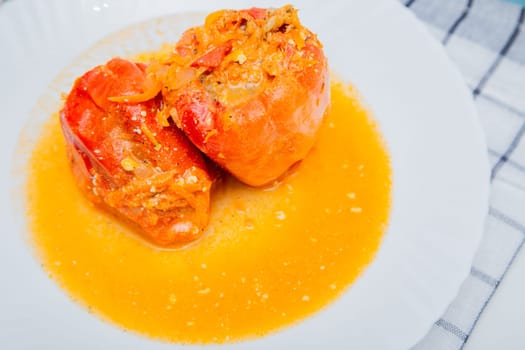Red pepper stuffed with minced meat and carrots with onions lies on a white plate, which stands on a waffle napkin on a white background. High quality photo