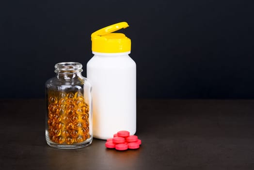A glass jar with bright yellow tablets and a white pill jar on a brown background. Place for the label, logo, layout.