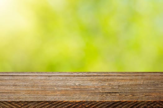 Background with blurred green leaves and empty wooden planks in the foreground. For product demonstrations, free space, layout, mockup, perspective board, background board.