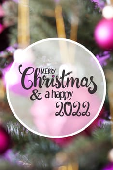 English Calligraphy Merry Christmas And Happy 2022. Pink Christmas Ball Ornament On Christmas Tree