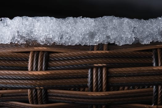 Layer of ice sits on top of textured plastic garden furniture. Copy space over black backgruond, full frame composition. Rope like macro appearance