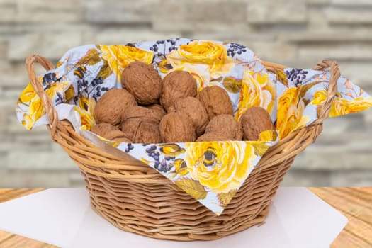 A wicker basket with a napkin full of walnuts on a table in front of an abstract, blurry brick wall. Macro. Concept of healthy eating.