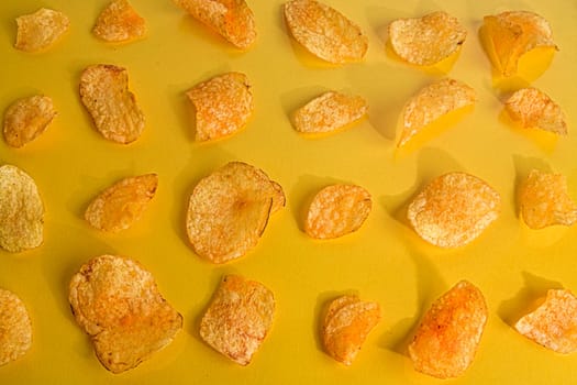 Close-up of potato chips or crisps on pastel yellow background.  Cinema concept with many potato chips on yellow retro background.