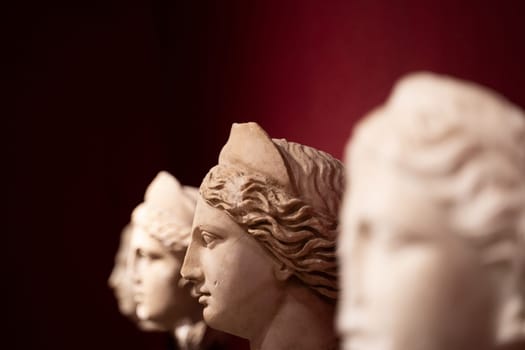 perspective view closeup of woman antique statues heads arranged in row on red background