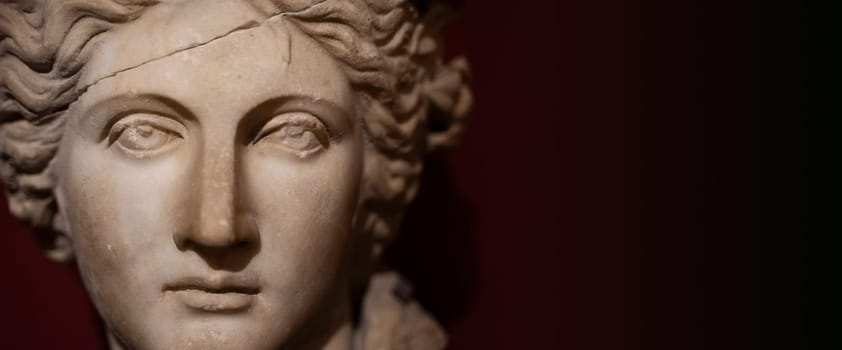 front view closeup of woman antique white marble statue with cracked forehead face and damaged eyes on dark background copy space available