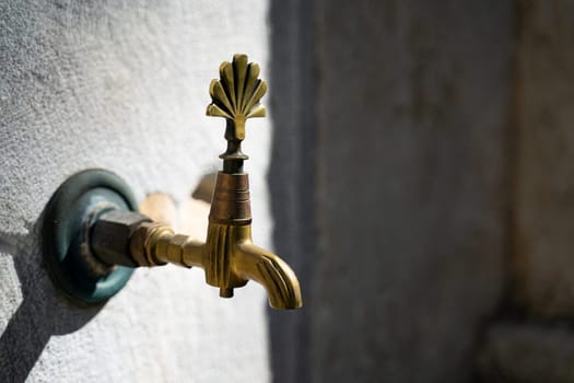 closeup of vintage bronze water faucet with decorated tap next to a Muslim mosque with stone background