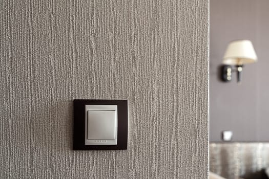 front view closeup of white light plastic switch socket on textured wall with home interior in the background