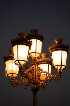 closeup view of vintage old street light with iron arms shining in the night