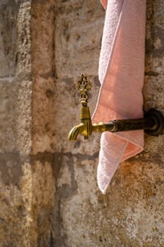 closeup of vintage bronze water faucet with decorated tap and bath towel next to a Muslim mosque with stone background