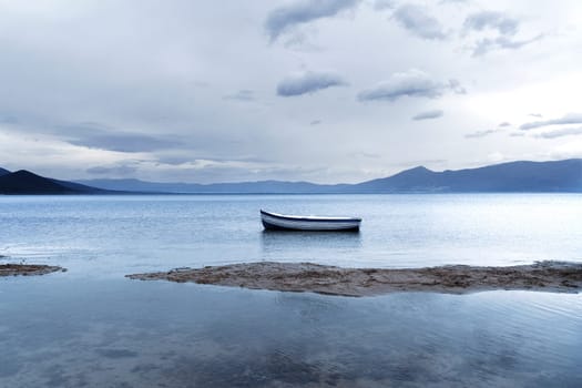 natural landscape with mountains and lonely boat with blue and white stripes on lake Prespa in North Macedonia