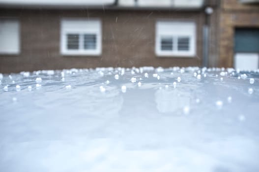 Hail falling over car roof. Selective focus over urban background
