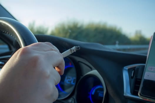 Woman smoking while she is driving. Cause of distracted driving accidents concept. Inside car view