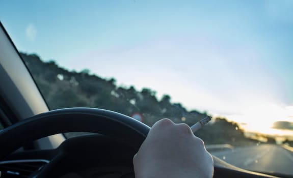 Woman smoking while she is driving. Cause of distracted driving accidents concept. Inside car view