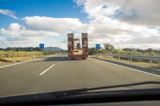 Heavy-duty truck with folded platform driving empty. View from the inside of the car