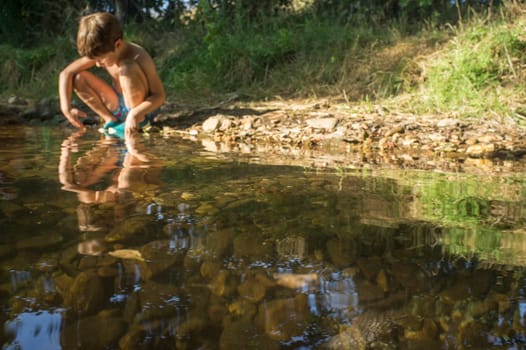 Little boy exploring clear mountain riverside. Selective focus on riverbed