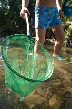 Little boy playing with fishing net in the river. Holidays where kids can go wild concept