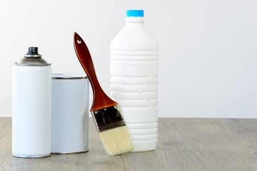 bottle, aerosol, paint pot and brush on wooden table